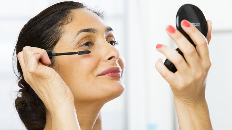 Woman applying mascara and looking in compact mirror