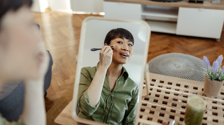 Woman applying makeup in mirror