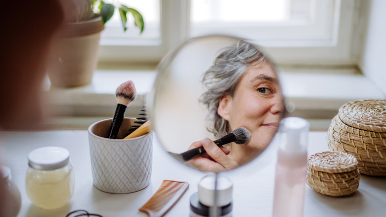 Woman applying makeup with brush looking in mirror