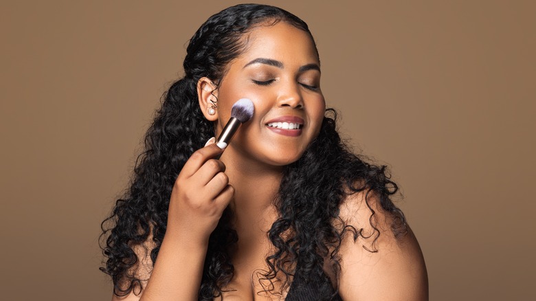 Woman holding makeup highlighter to cheek and smiling