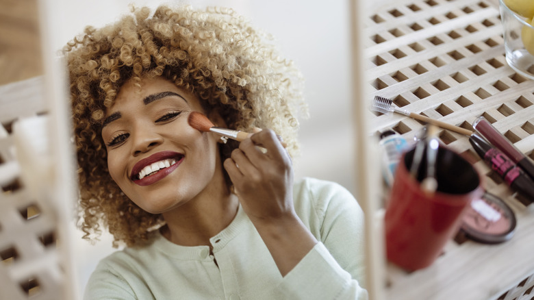 Woman smiling as she applied makeup powder in the mirror