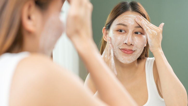 Woman looking in mirror as she exfoliates her face