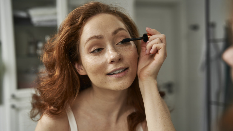 Woman applying mascara in the mirror