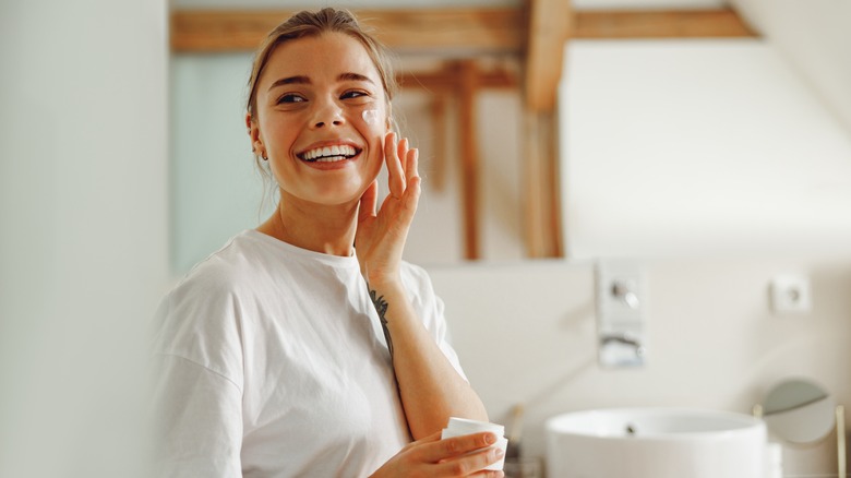 Woman smiling applying lotion to her cheek