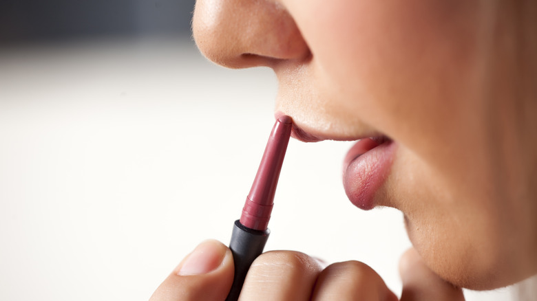 Woman applying pink lip liner to top lip