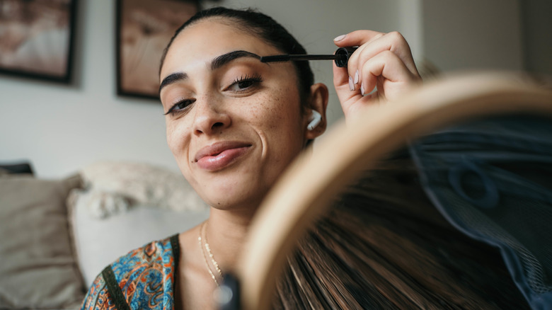 Woman smiling in mirror holding mascara brush