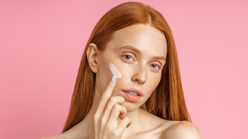 A woman applying cream on her face