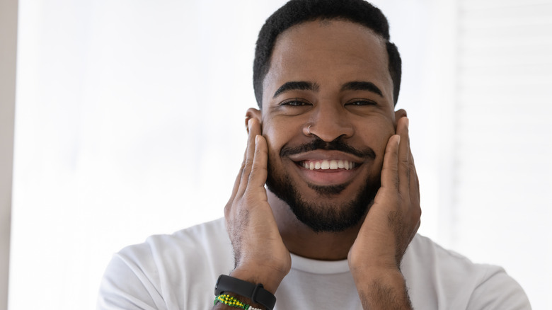 A smiling man touching his face with his hands 