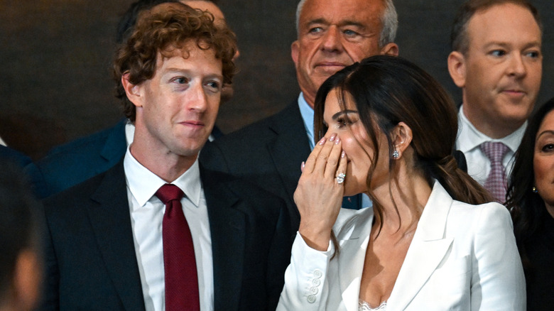 Mark Zuckerberg smirking next to Lauren Sanchez covering her face