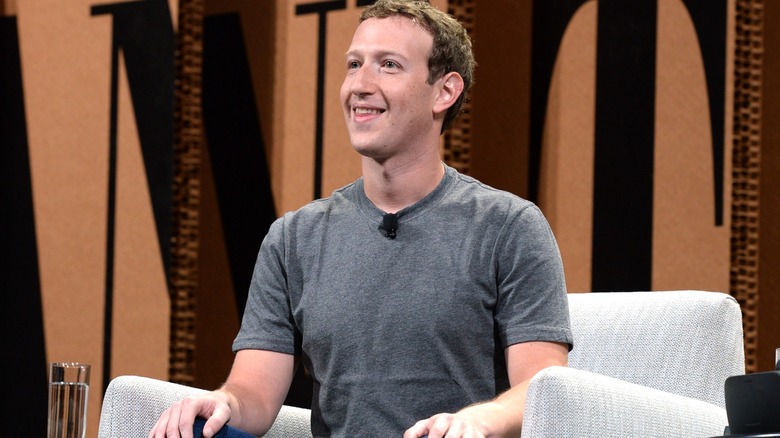 Mark Zuckerberg sitting in a chair with his hands on his knees, smiling upward