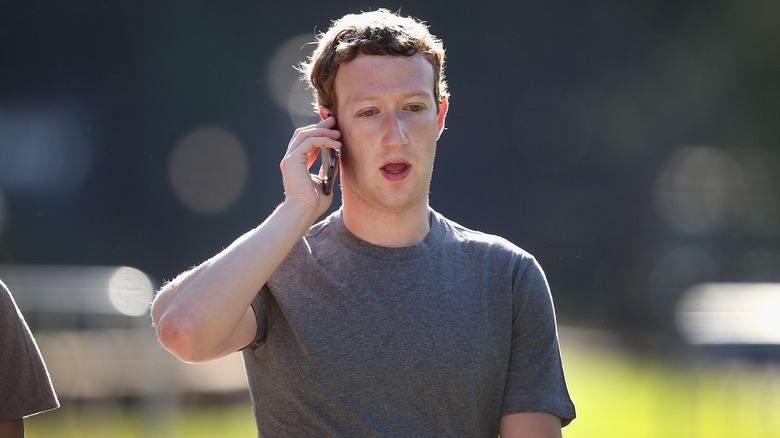 Mark Zuckerberg in a grey t-shirt holding a cell phone to his ear, looking shocked