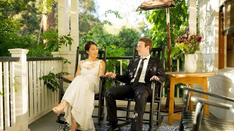 Mark Zuckerberg and Priscilla Chan on their wedding day in a white dress and a suit, holding hands in rocking chairs