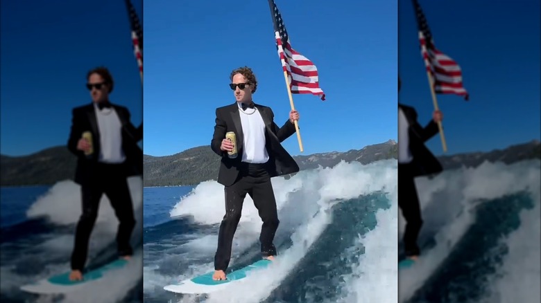 Mark Zuckerberg barefoot on a surfboard holding an American flag