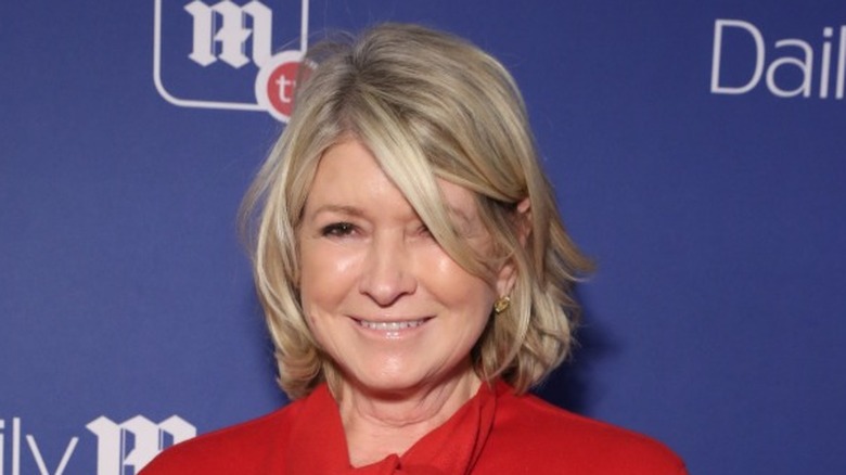 Martha Stewart on red carpet wearing red blouse, hair disheveled and covering face.