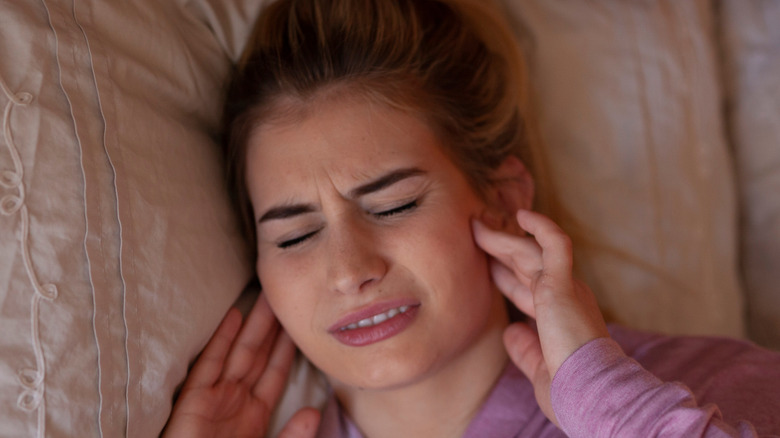 woman laying in bed touching jaw in pain