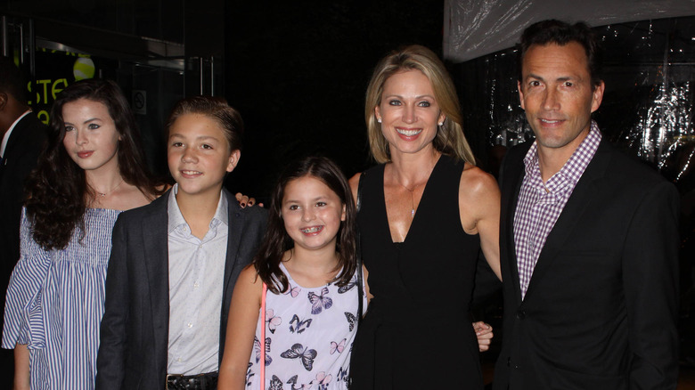 Amy Robach stands with her arms around young Ava and Annalise McIntosh and stepson next to Andrew Shue