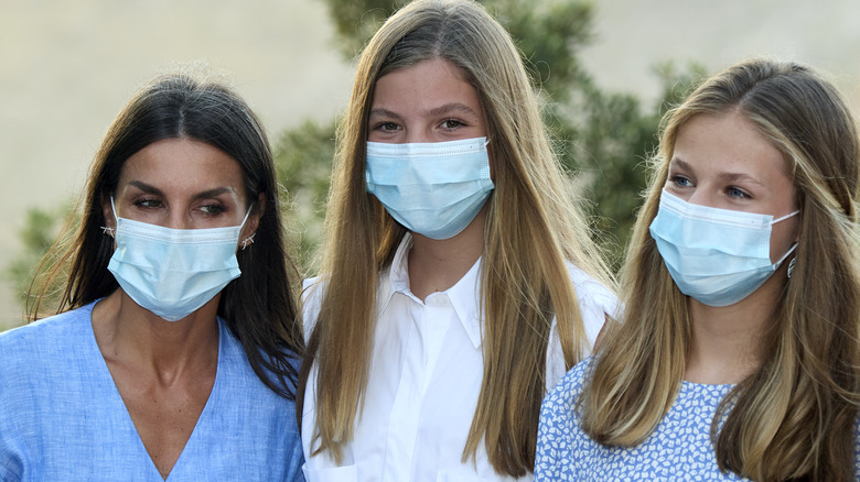 Queen Letizia, Infanta Sofía, and Princess Leonor smiling under face masks