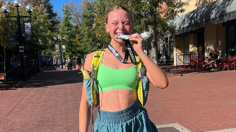 Adelyn Dozier stands in Boulder after a marathon with her runner's tag in her mouth