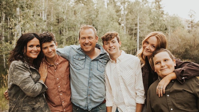 The Dozier family stands smiling with arms around each other in the woods