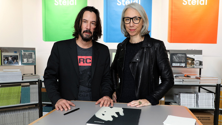 Keanu Reeves and Alexandra standing next to their publication "Ode to Happiness" in 2017