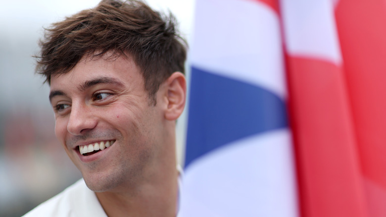 Tom Daley smiling next to U.K. flag