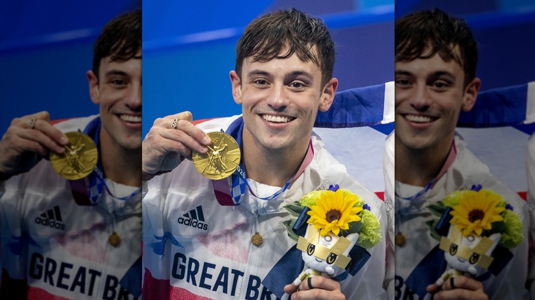 Tom Daley smiles holding flowers and gold medal