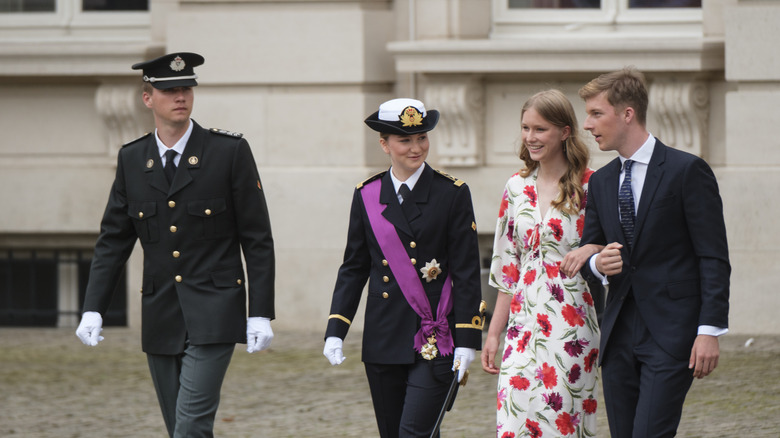 The four royal children of Belgium walk together on a cobble street.