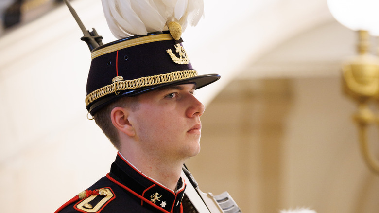 Prince Gabriel walks in military garb carrying a rifle.