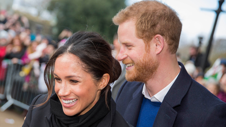 Prince Harry and Meghan Markle smiling and greeting the crowd together