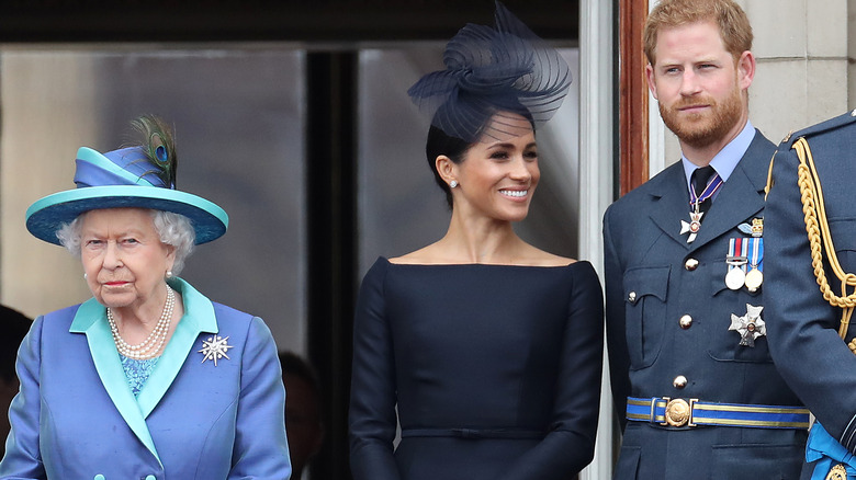 Meghan Markle and Prince Harry smile while the queen looks grumpy