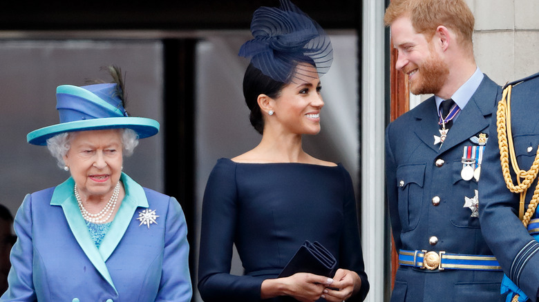 Meghan Markle and Prince Harry smiling at each other next to the queen