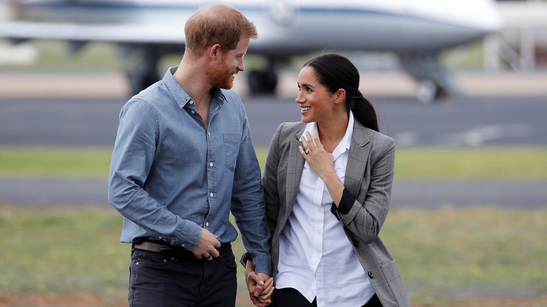 Prince Harry and Meghan Markle looking at each other with a plane in the background