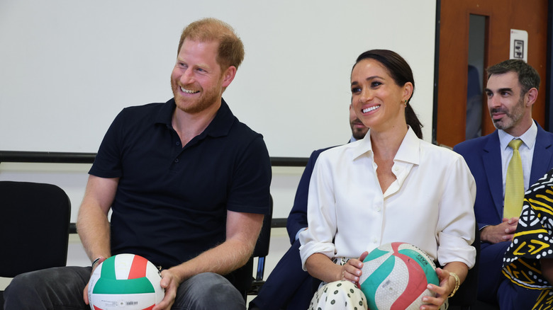 Prince Harry and Meghan Markle holding soccer balls while smiling