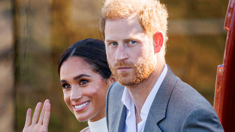 Meghan Markle waves to fans while Prince Harry looks on