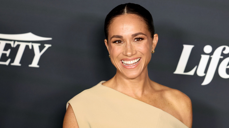 Meghan Markel smiles in a beige outfit at an event