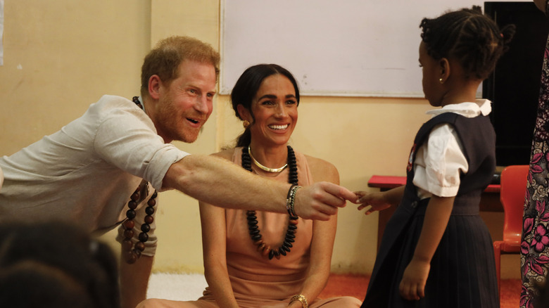 Prince Harry and Meghan Markle smiling at a child