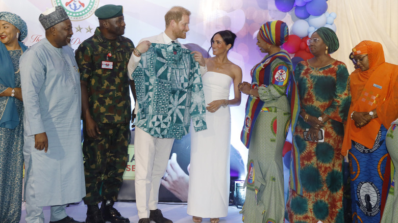 Prince Harry holding up traditional Nigerian shirt with Meghan Markle