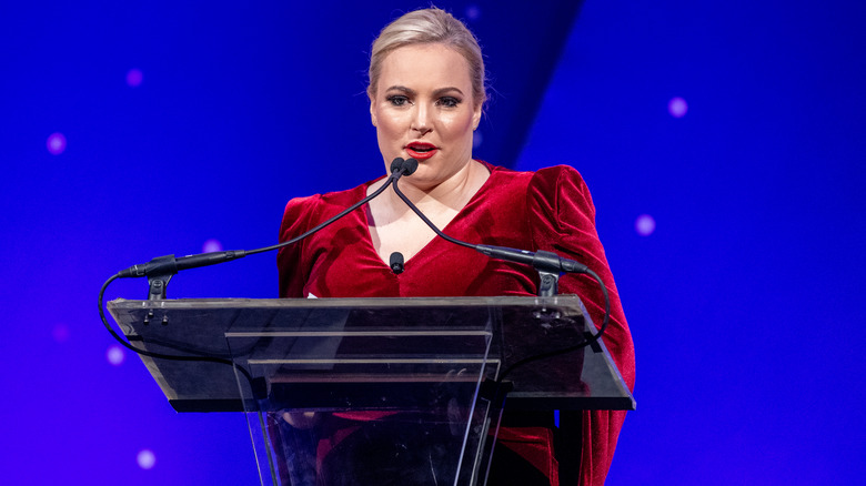 Meghan McCain stands on stage in a velvet red dress.