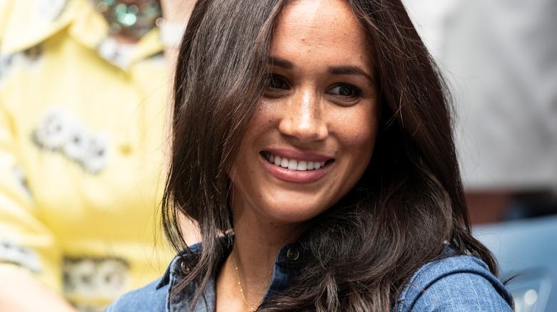 Meghan Markle smiling and wearing a denim shirt