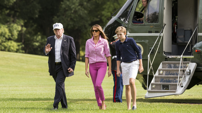 Melania, Donald, and Barron Trump walking across lawn after leaving helicopter