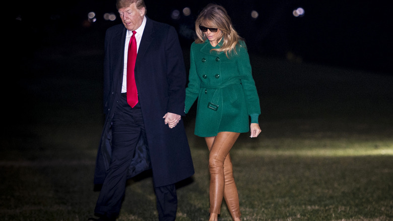 Melania and Donald Trump holding hands walking across lawn