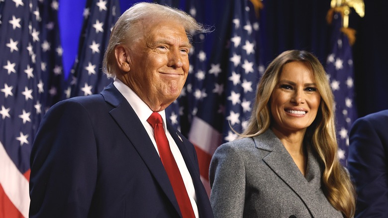 Donald and Melania Trump smiling near American Flags