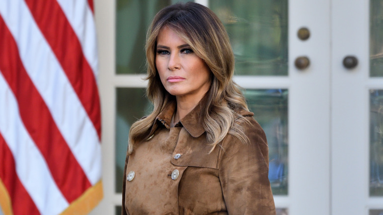 Melania Trump wearing brown jacket looking serious