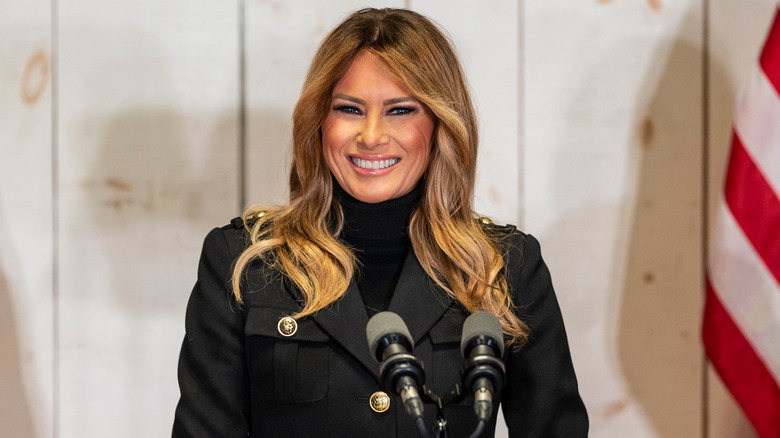 Melania smiling behind a pair of microphones