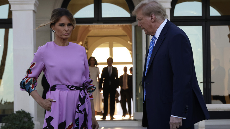 Melania Trump hand in pocket purple jumpsuit looking serious Donald trump turned toward her