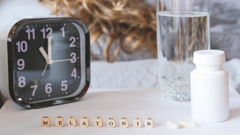 A clock, glass of water, and bottle of melatonin on a nightstand