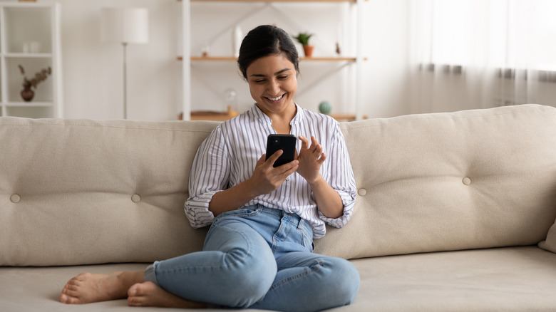 woman sitting on a coach surfing her phone