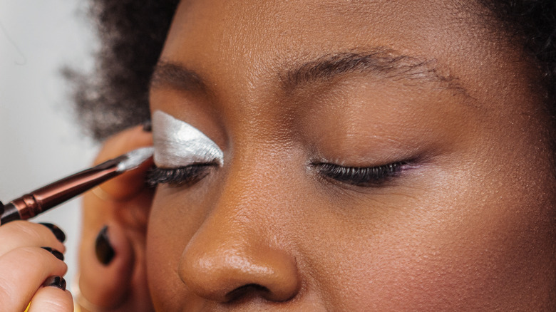 Makeup artist applying liquid silver eyeshadow on model