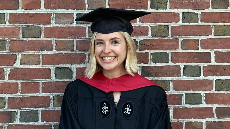 Schuyler Fox smiling in graduation robes against brick wall