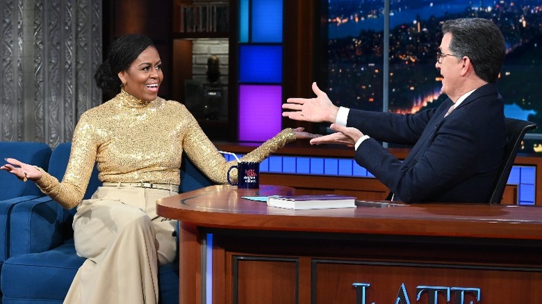 Michelle Obama in gold outfit talks to Stephen Colbert